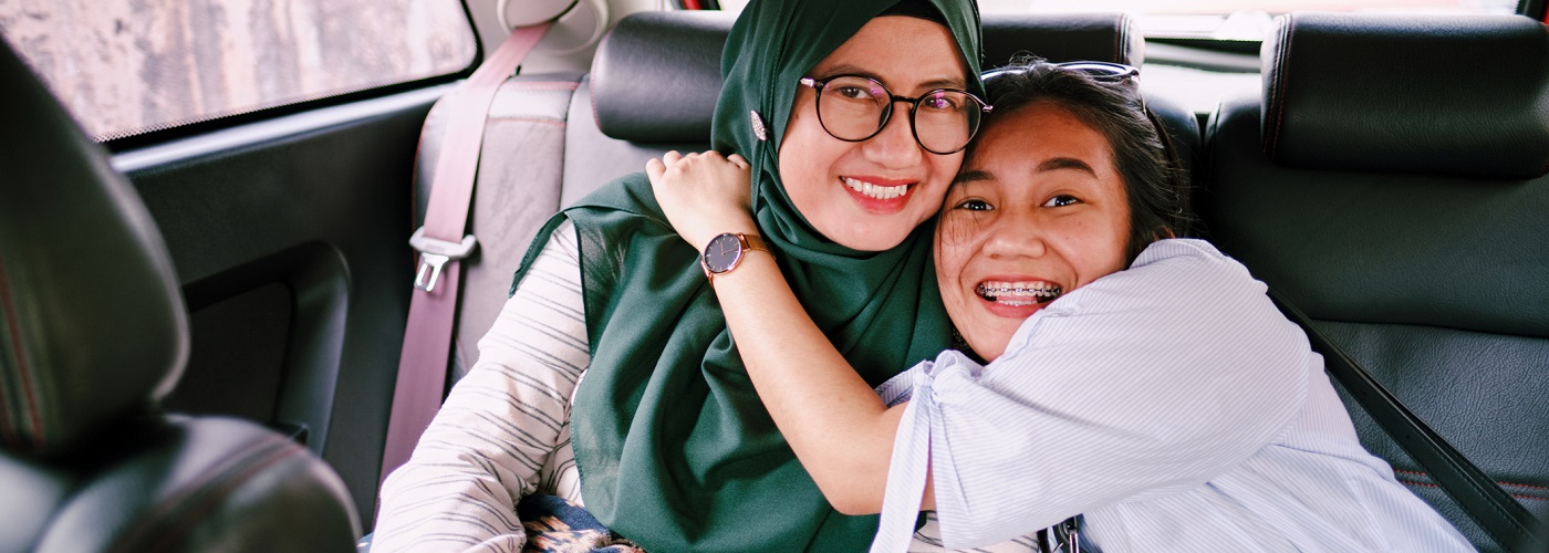 A mother and daughter smiling and hugging in a car