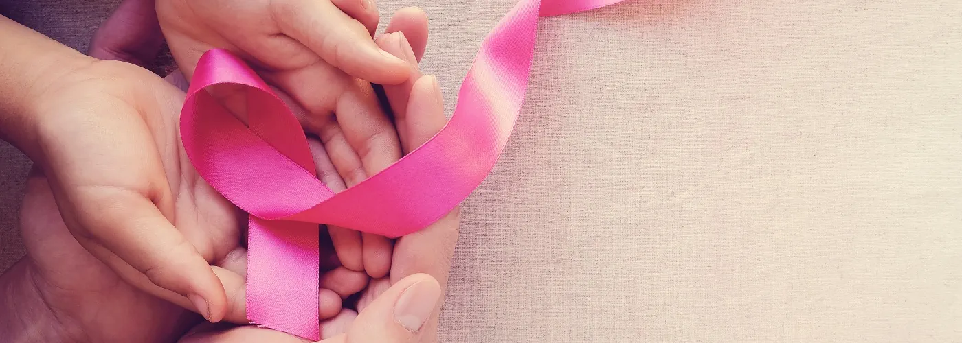 two hands holding a pink ribbon, representing breast cancer care